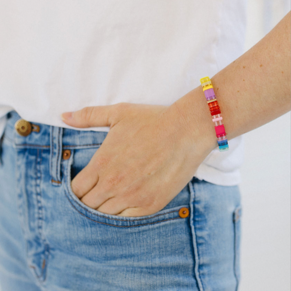 Picture of a woman with her hand in her pocket. She is wearing a beaded bracelet in yellows, purples, reds and blues.