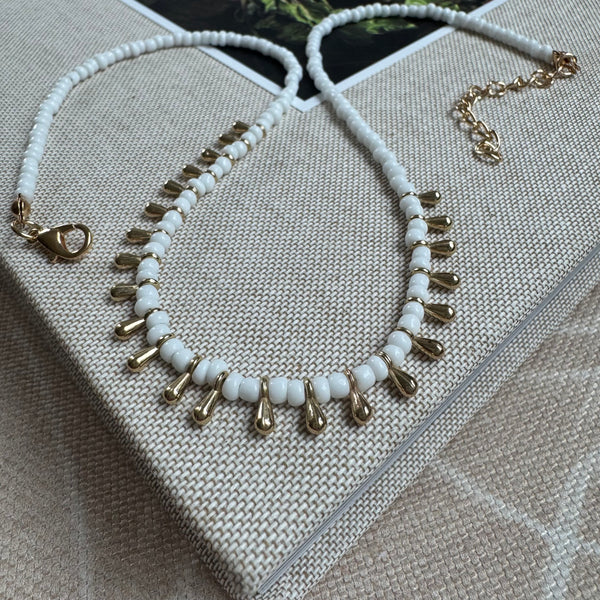 Picture of a white bead necklace with gold teardrop beads alternating through it's center.