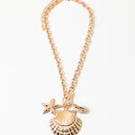 Picture of a gold chain necklace with three large sea pendants. Pendants are a large clam seashell, a smaller gold starfish and a small cowry shell.