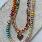 Set of three necklaces made up of small colorful bead necklace, a gold chain link with hammered gold heart pendant and a larger colorful beaded necklace.