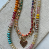 Set of three necklaces made up of small colorful bead necklace, a gold chain link with hammered gold heart pendant and a larger colorful beaded necklace.