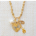 Picture of gold toggle chain with a large gold heart pendant with a diamond in the center. Three additional charms are attached. One is a fresh water pearl, one a gold horseshoe and one a gold teardrop with a small diamond at the center.