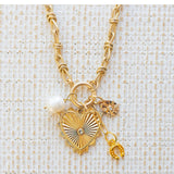 Picture of gold toggle chain with a large gold heart pendant with a diamond in the center. Three additional charms are attached. One is a fresh water pearl, one a gold horseshoe and one a gold teardrop with a small diamond at the center.