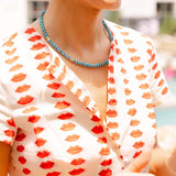 Woman outside wearing a white dress with a red lips print and a blue/gold beaded necklace around her neck