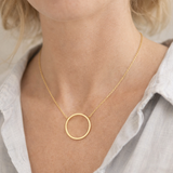 Gold necklace with a circular pendant worn by a person in a light-colored shirt.