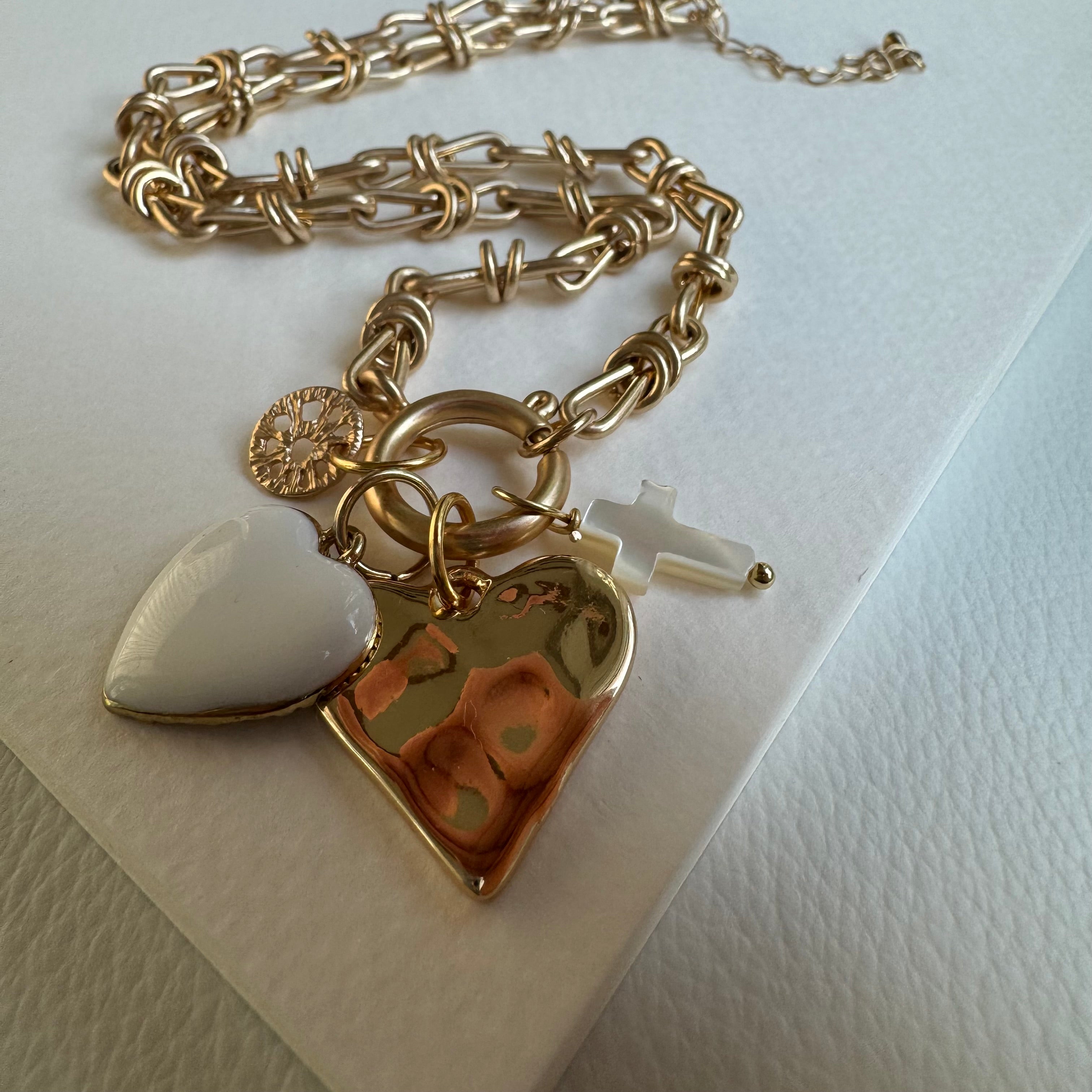 Picture of chunky gold chain necklace with a large gold heart pendant. Necklace also has three other charms, a gold paw print, a white cross and a white heart
