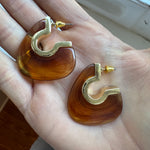Resin amber brown earrings with gold hooks held in a hand.