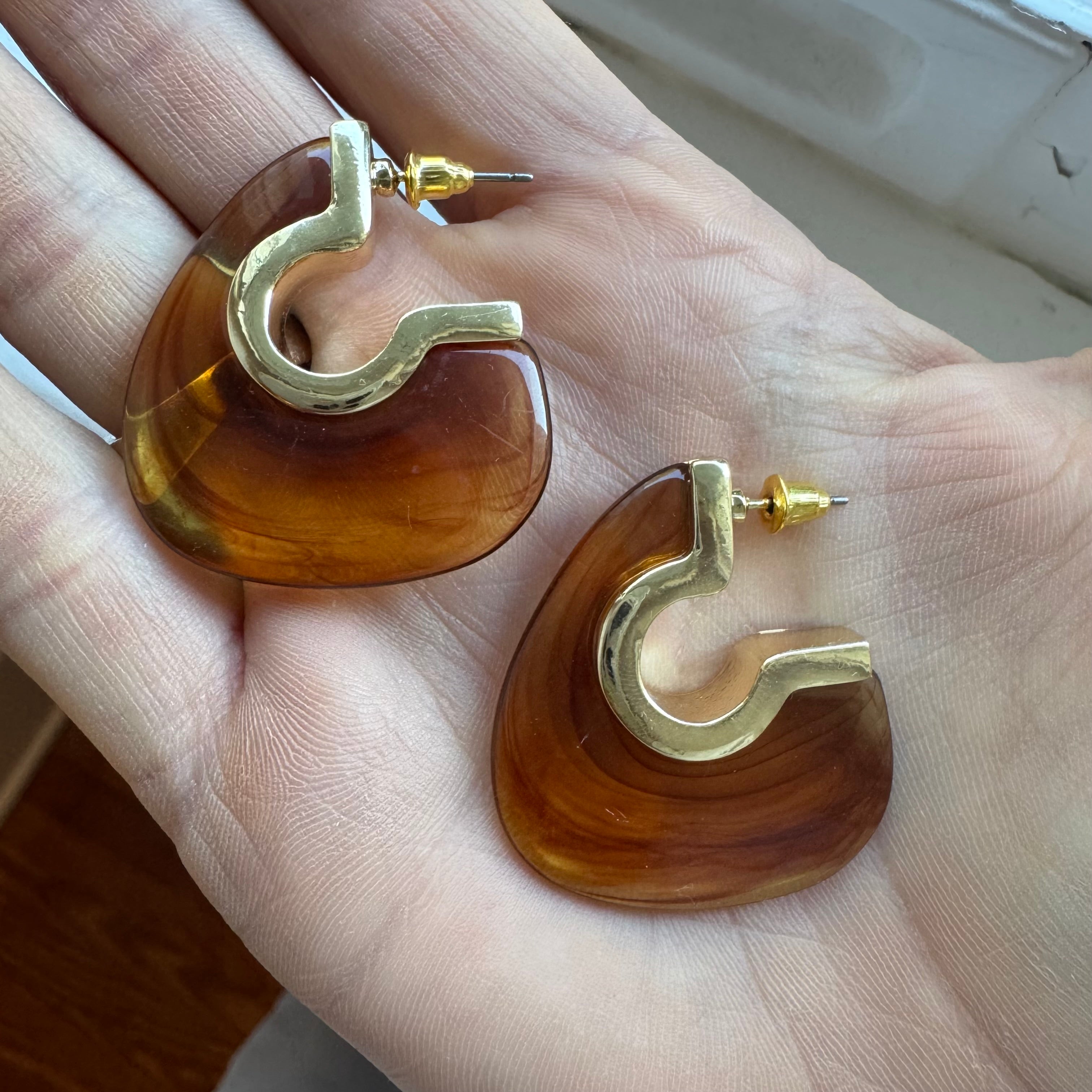 Resin amber brown earrings with gold hooks held in a hand.