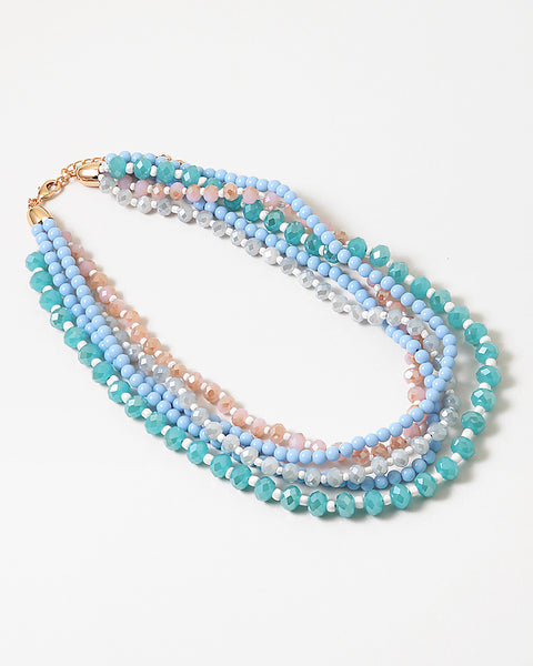 An image of layered beaded necklaces (blue, green, and pink) stacked on each other