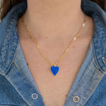 Person wearing a gold chain with a blue enamel heart pendant