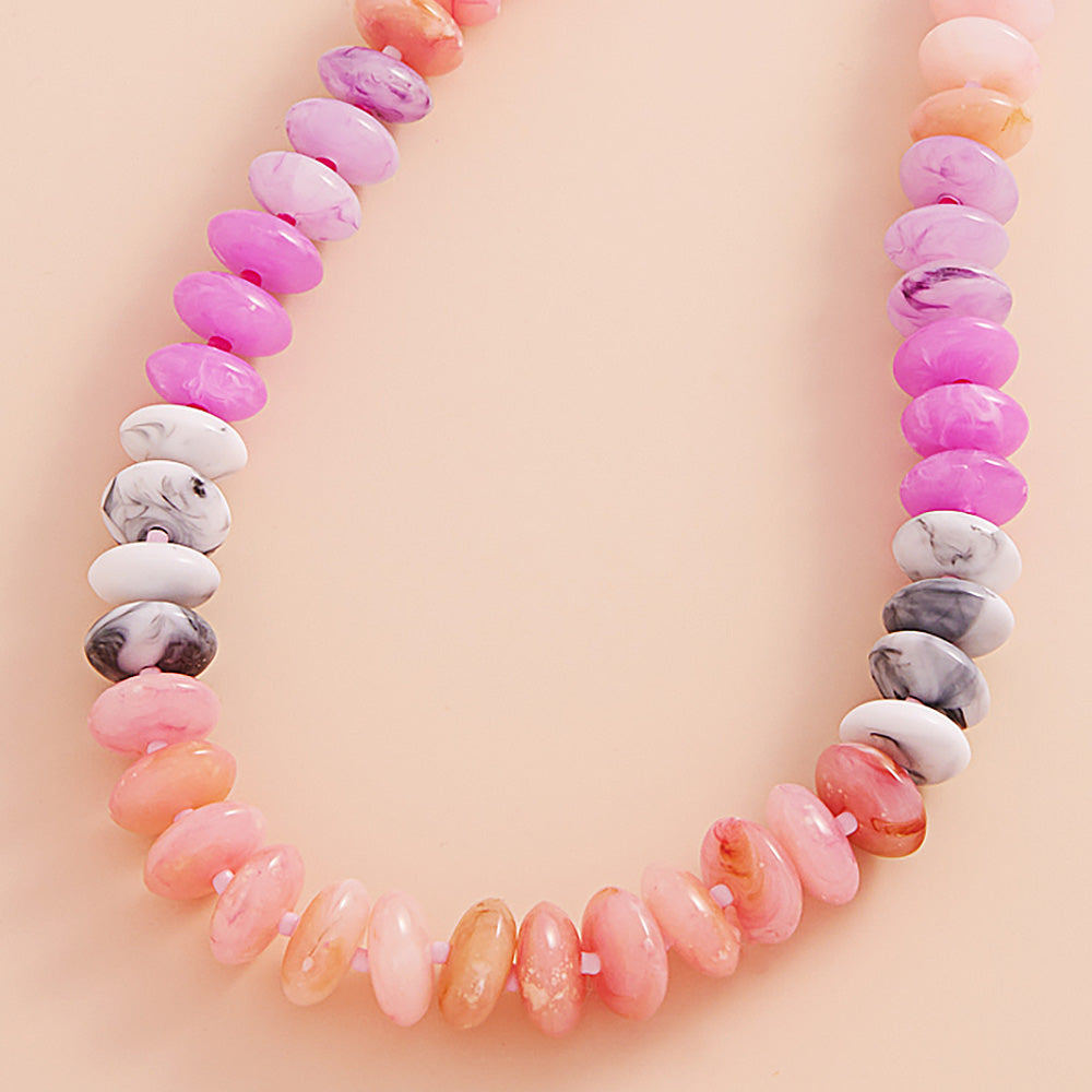Necklace with multicolored beads in pink, white marble and coral on a light pink background