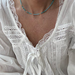 Picture of a model wearing a white lacy blouse and a delicate teal necklace with gold spacer beads.