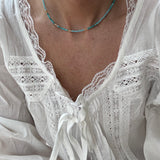 Picture of a model wearing a white lacy blouse and a delicate teal necklace with gold spacer beads.