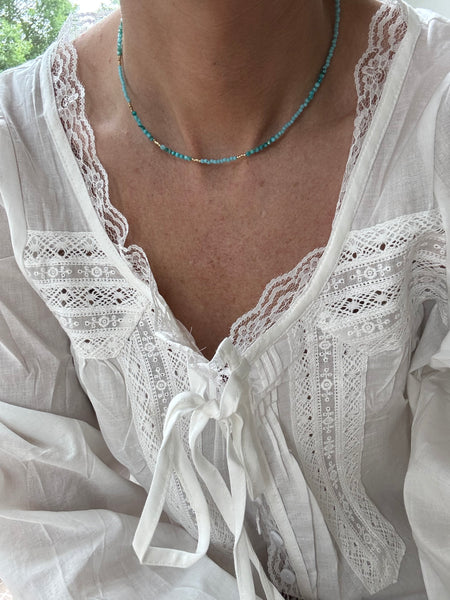 Picture of a model wearing a white lacy blouse and a delicate teal necklace with gold spacer beads.