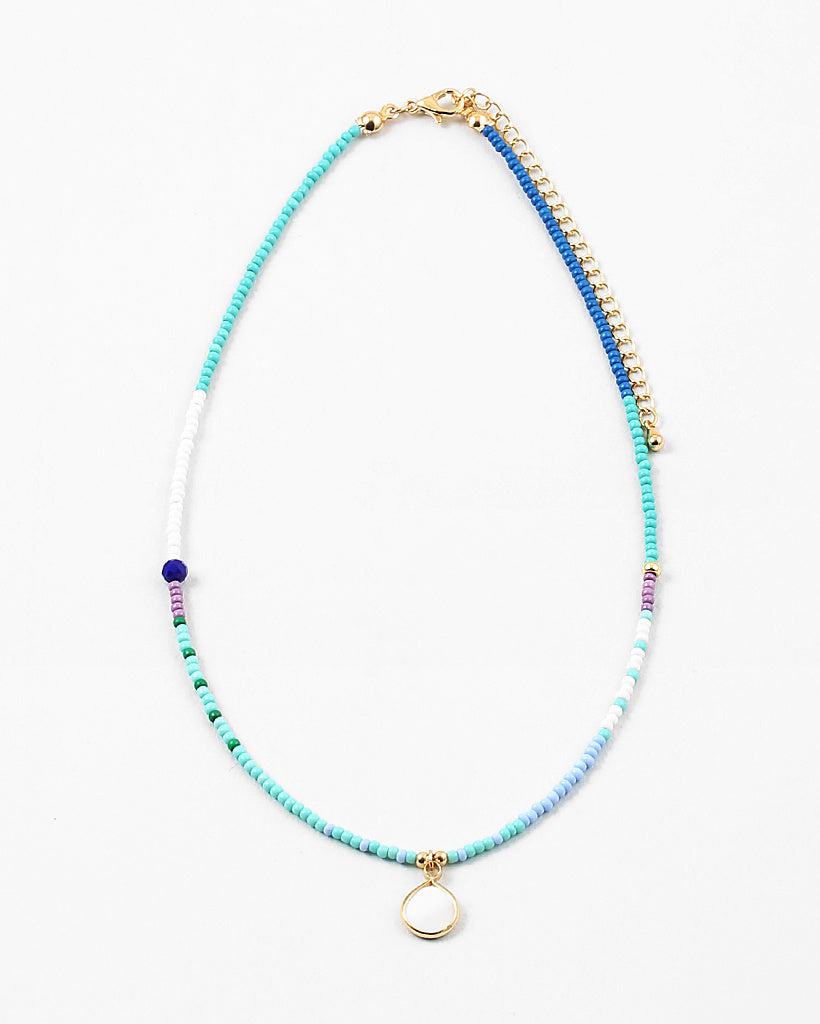 Necklace with blue, white and gold beads with a small white enamel pendant on a white background