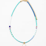 Necklace with blue, white and gold beads with a small white enamel pendant on a white background