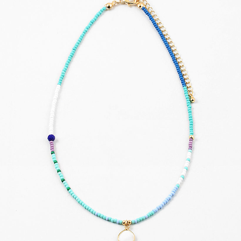 Necklace with blue, white and gold beads with a small white enamel pendant on a white background