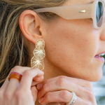 Woman wearing sunglasses reaching for her gold circular/stacked on each other sand dollar earring 