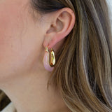 Picture of a woman wearing gold hoop earrings with rose pink resin on the outside of it. 