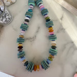 Necklace with multicolored beads and teal wooden disc beads on a marble surface