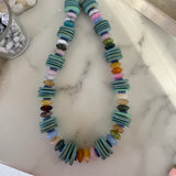 Necklace with multicolored beads and teal wooden disc beads on a marble surface