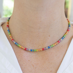 Model wearing a delicate necklace with red, orange, yellow, green, blue and purple beads that have tiny gold spacers in between each.