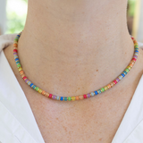 Model wearing a delicate necklace with red, orange, yellow, green, blue and purple beads that have tiny gold spacers in between each.