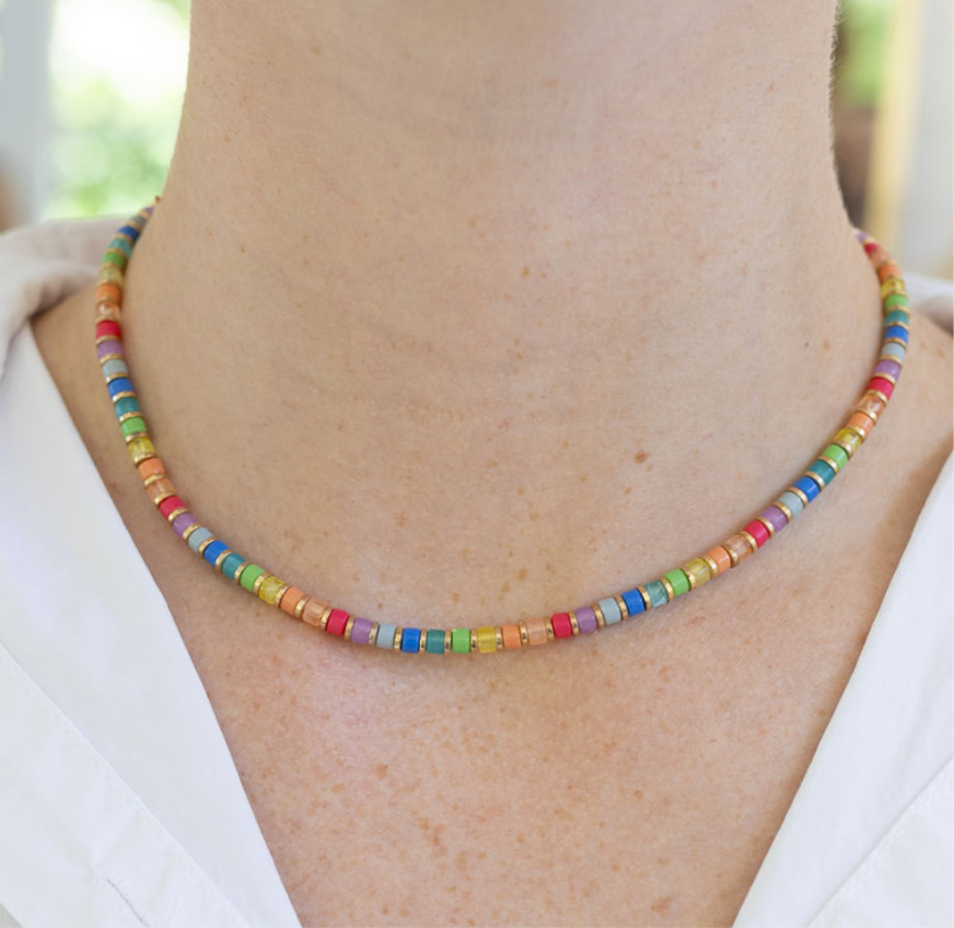 Model wearing a delicate necklace with red, orange, yellow, green, blue and purple beads that have tiny gold spacers in between each.
