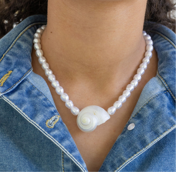 Pearl necklace with a shell pendant worn by a person in a denim jacket.