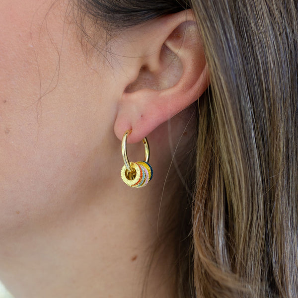 Picture of woman wearing small gold hoops. Dangling from them are multiple disc hoops.