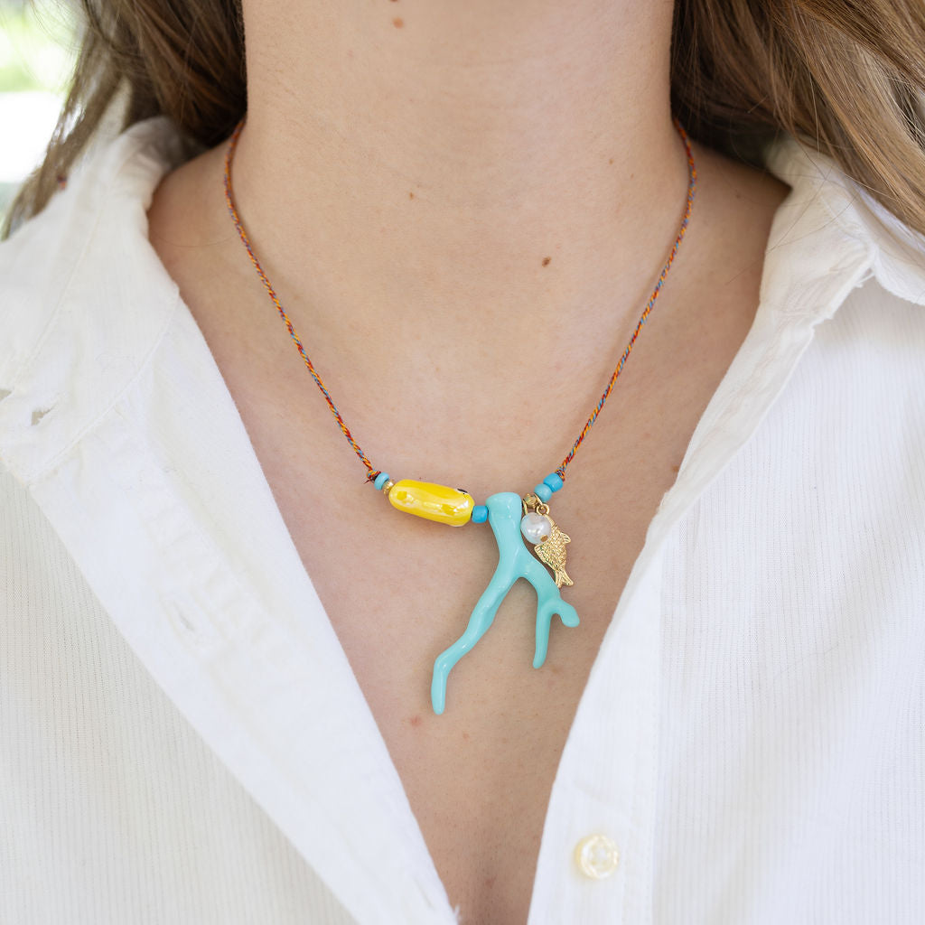 Picture of a twisted red and white string necklace with a large yellow oval bead, a light blue coral bead, a fresh water pearl and a small golden fish pendant.