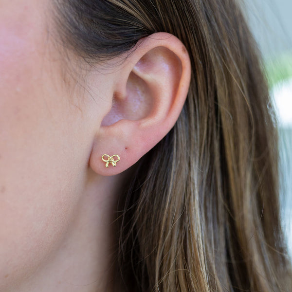 Picture of  woman wearing dainty gold bow earrings studs.