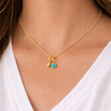 Gold necklace with a turquoise pendant and a small gold teardrop pendant on a person wearing a white top.
