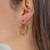 Picture of model wearing a gold hoops made of three strands of gold lightly woven together.