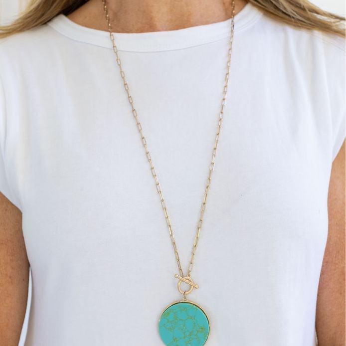 Picture of a woman wearing a long gold link chain with a large turquoise disc pendant.