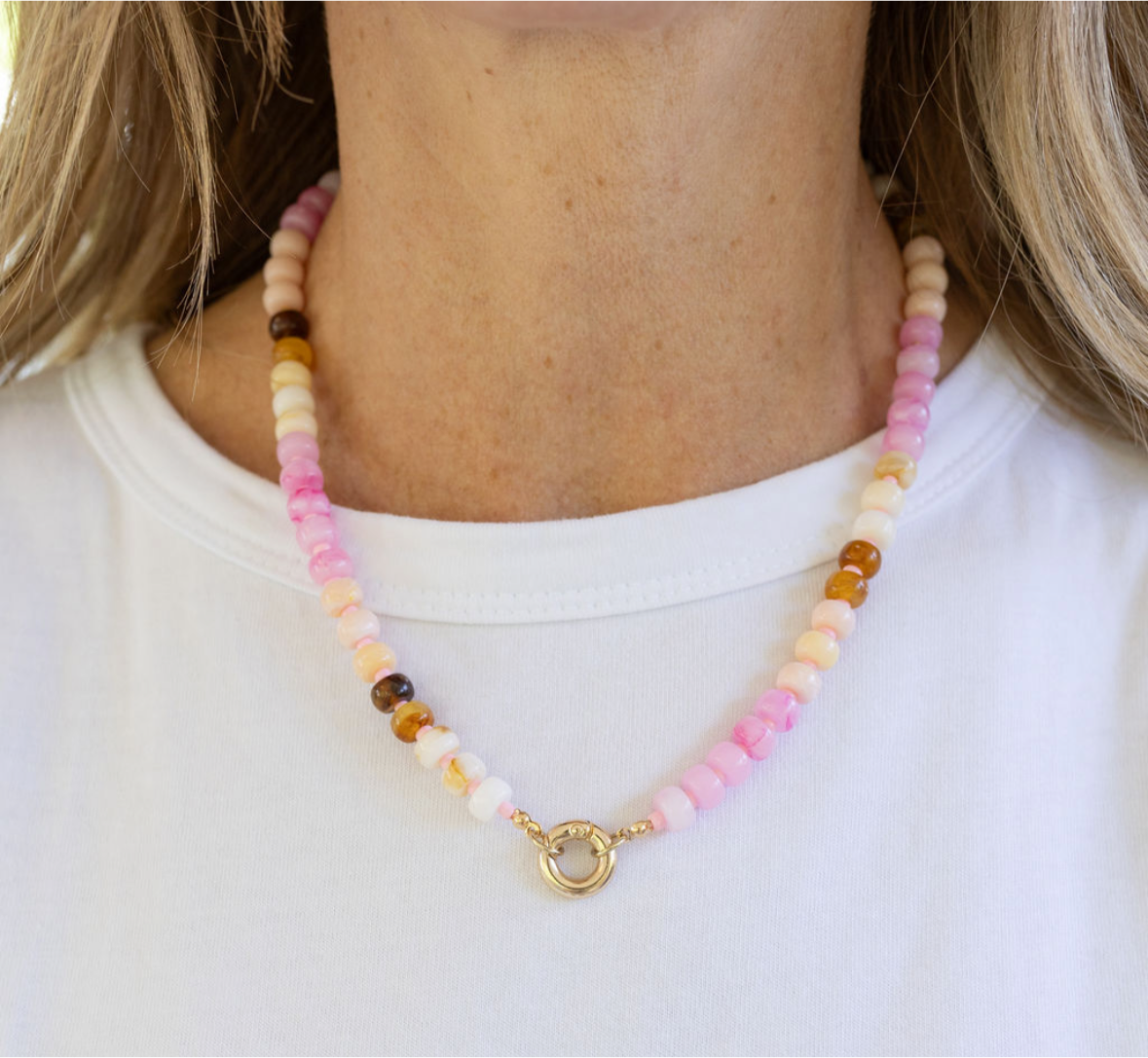 Necklace made of pink, beige and white beads with a large central gold clasp. 