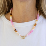 Necklace made of pink, beige and white beads with a large central gold clasp. 