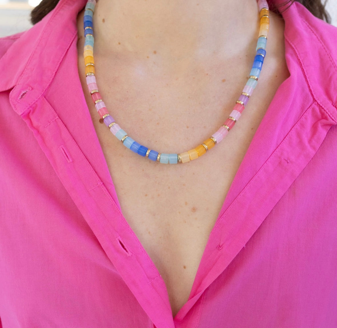 Picture of a woman wearing a pink shirt and a multicolored bead necklace in shades of pinks, blues and yellows.