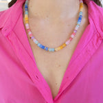 Picture of a woman wearing a pink shirt and a multicolored bead necklace in shades of pinks, blues and yellows.