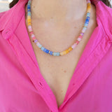 Picture of a woman wearing a pink shirt and a multicolored bead necklace in shades of pinks, blues and yellows.