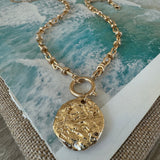 A gold chunky chained necklace sitting on a table with a large gold medallion attached to it
