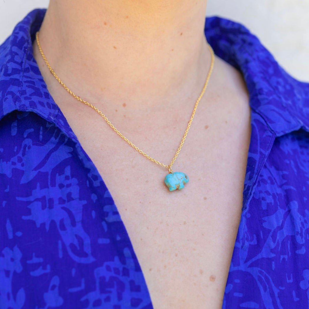 Picture of model wearing a a blue shirt and a fine gold chain with a blue turquoise elephant pendant.