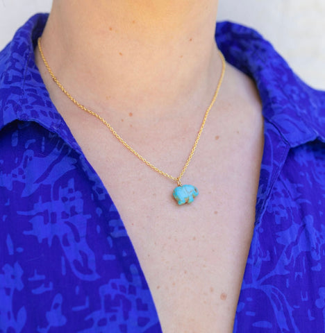 Picture of model wearing a a blue shirt and a fine gold chain with a blue turquoise elephant pendant.