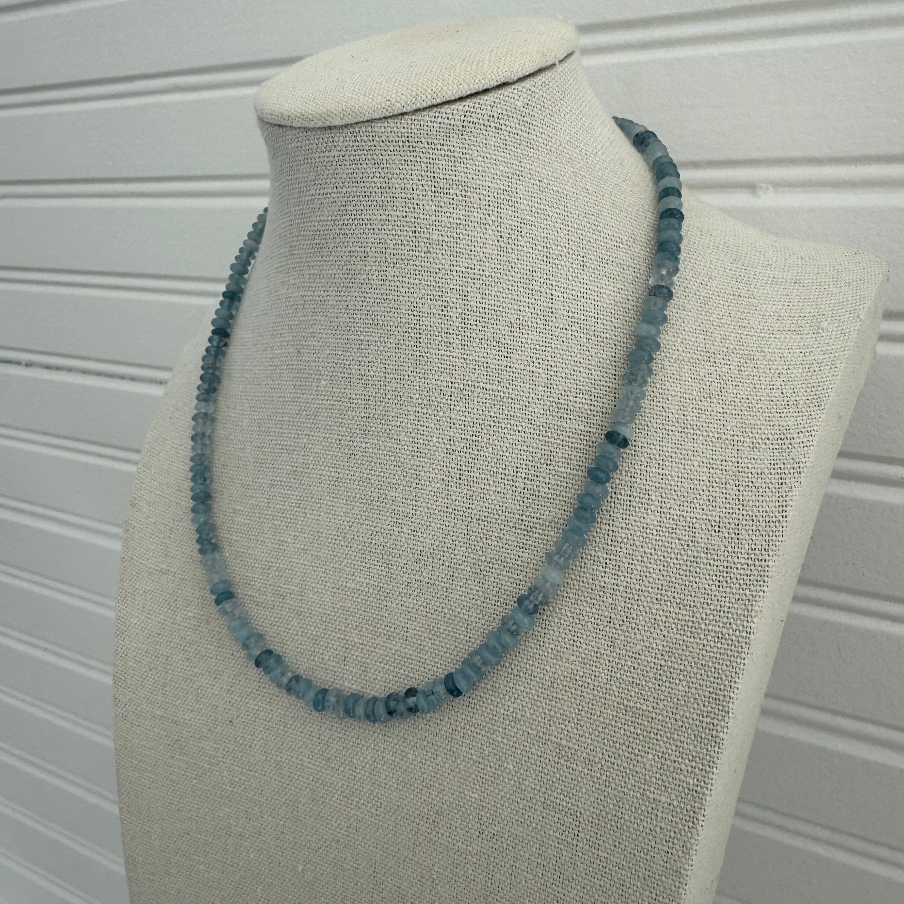 Picture of a display showing a slate blue bead necklace.