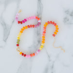 Colorful beaded necklace in oranges, yellows and pinks on a marble surface