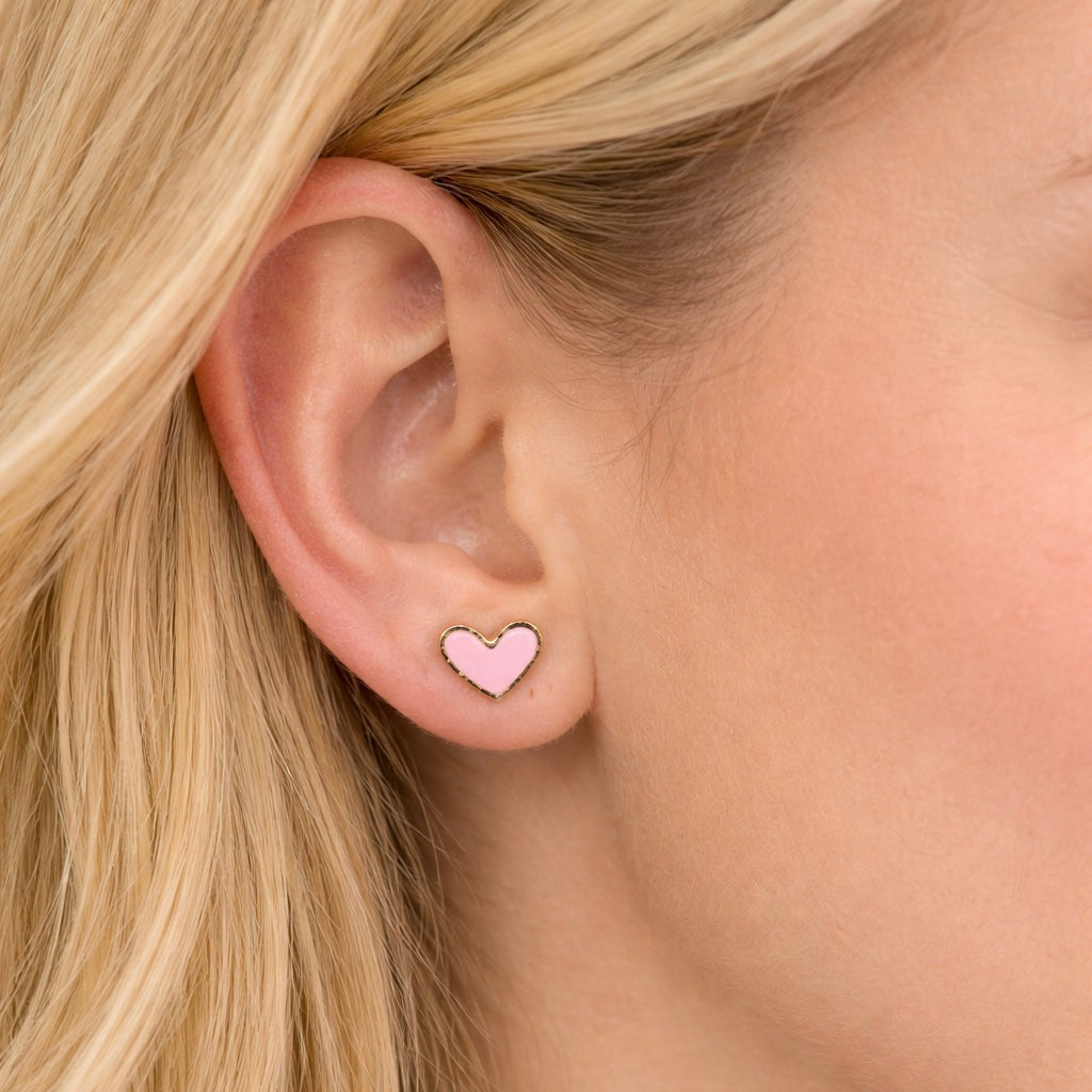 Close-up of an ear wearing a pink heart-shaped earring with blonde hair.