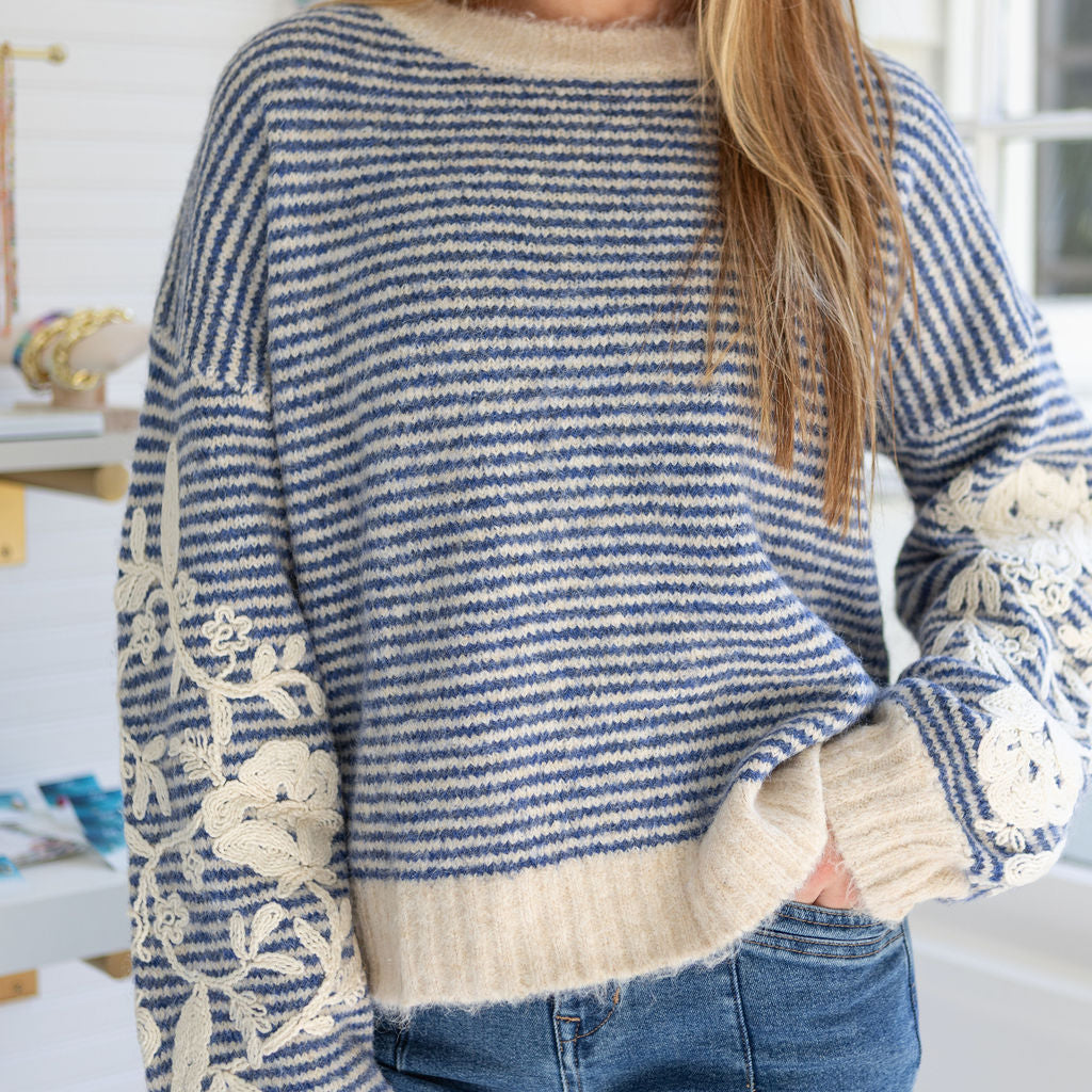 Person wearing a blue and white striped sweater with floral details in a casual setting.