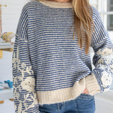 Person wearing a blue and white striped sweater with floral details in a casual setting.