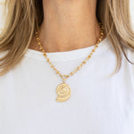 Picture of a woman wearing a gold chain necklace with a large gold spiral seashell pendant.