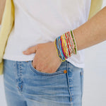 Picture of woman wearing eighteen different tiny bead bracelets. Bracelets are in shades of yellow, greens, blues and pinks.